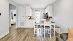 Eine moderne Küche mit weißen Schränken, einem Esstisch mit vier Stühlen und einem sichtbaren Kühlschrank.
