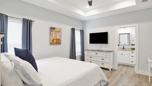 Ein Schlafzimmer mit Bett, Fernseher, Kommode und angrenzendem Badezimmer.