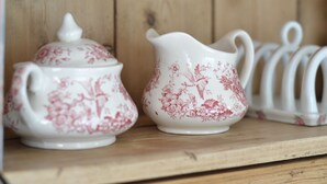 Una estant de fusta amb dos objectes de cuina de ceràmica, una tapa i una gerra, ambdós decorats amb motius florals.