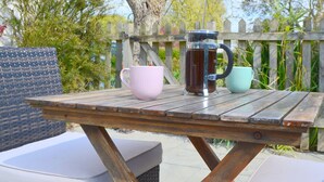 Una taula de fusta amb una french press, una tassa rosa i una altra color turquesa.