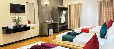 A hotel room with two beds, a TV, a mirror, a ceiling fan, a robe hanging, and a small table with toiletries.