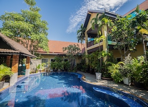 A swimming pool with a tiled edge, surrounded by lush greenery and a building with a red-tiled roof. - Sophavady D'Angkor (Siem Reap)