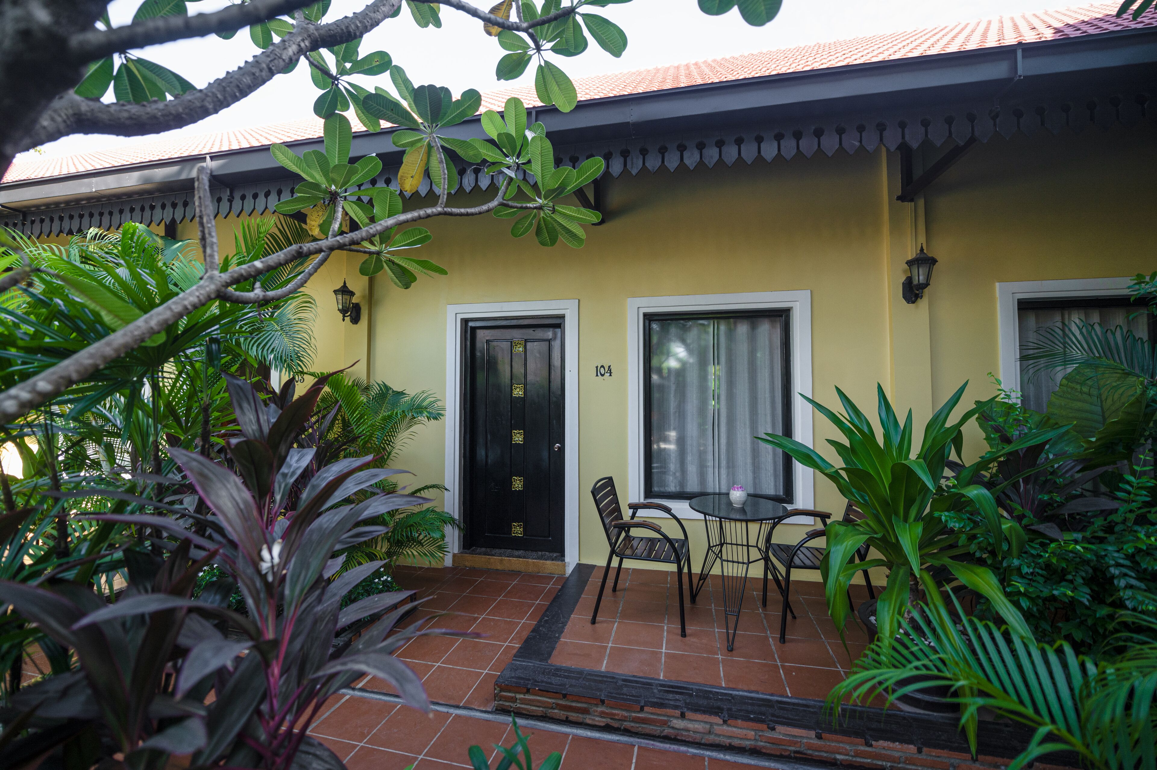 A yellow building with a tiled roof, two doors, and a small patio area with chairs and a table.