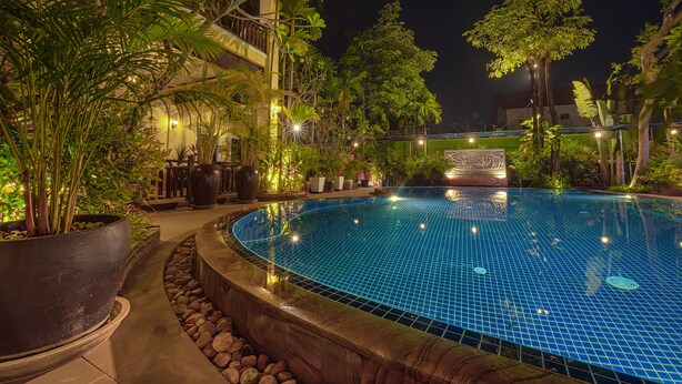 A nighttime swimming pool surrounded by tropical plants and a building with a sign. - Sophavady D'Angkor (Siem Reap)