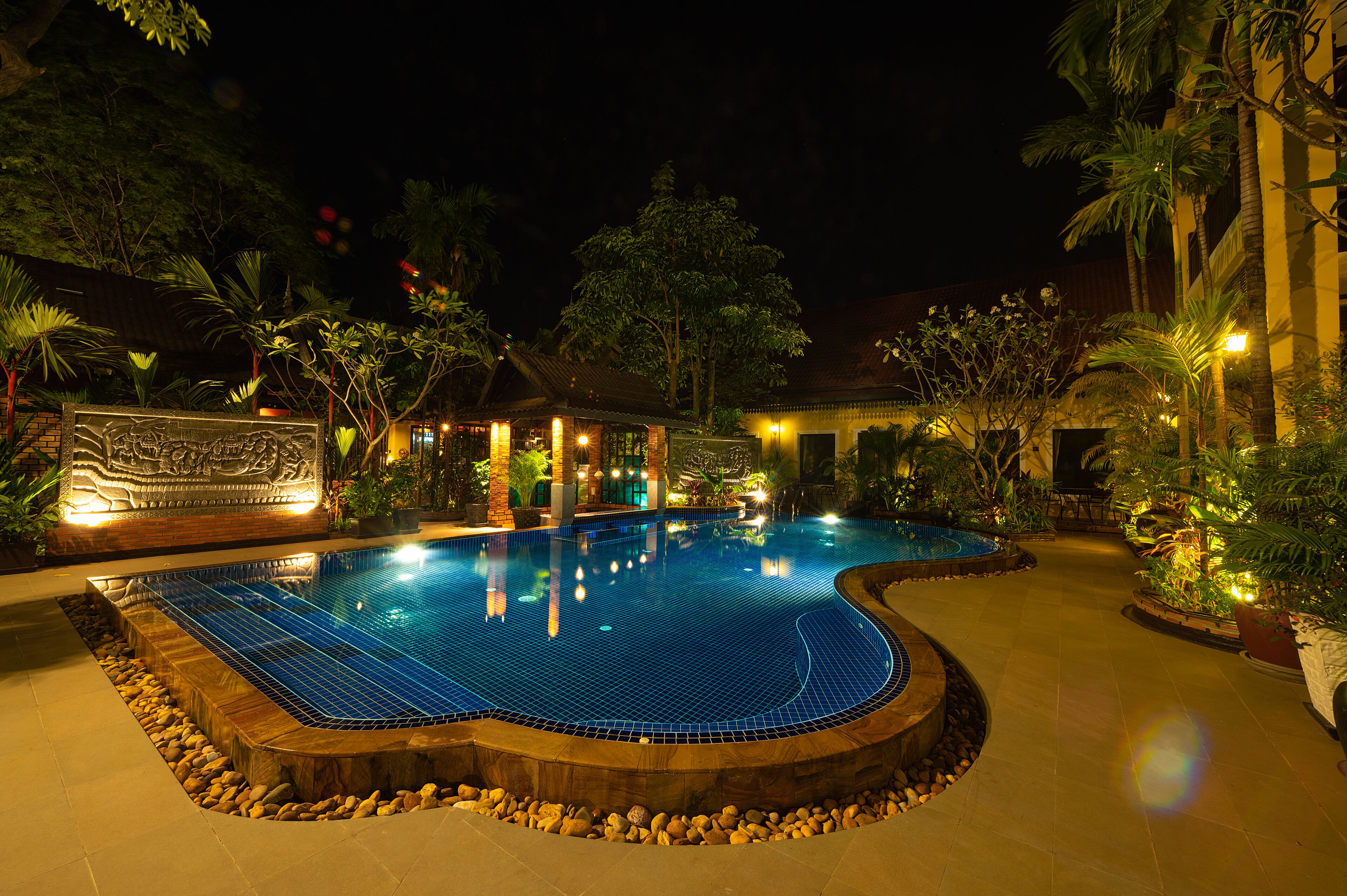 A swimming pool with a tiled deck, surrounded by rocks and plants.