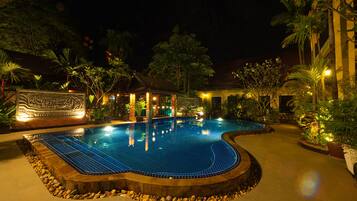 Piscina com deck ladrilhado, rodeada por pedras e plantas.