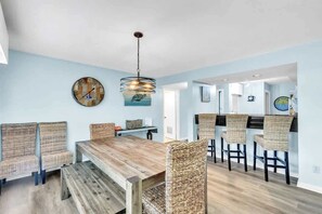 A dining area with a wooden table and wicker chairs, a hanging light fixture, and a clock on the wall. - Pet Friendly Villa, Pool Beach & Golf! Hilton Head (Hilton Head Island)