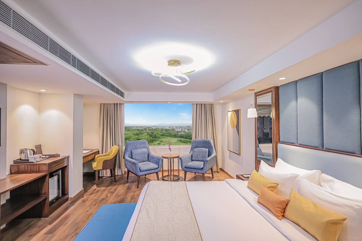 A hotel room with a bed, two armchairs, a desk, and a view of the landscape.