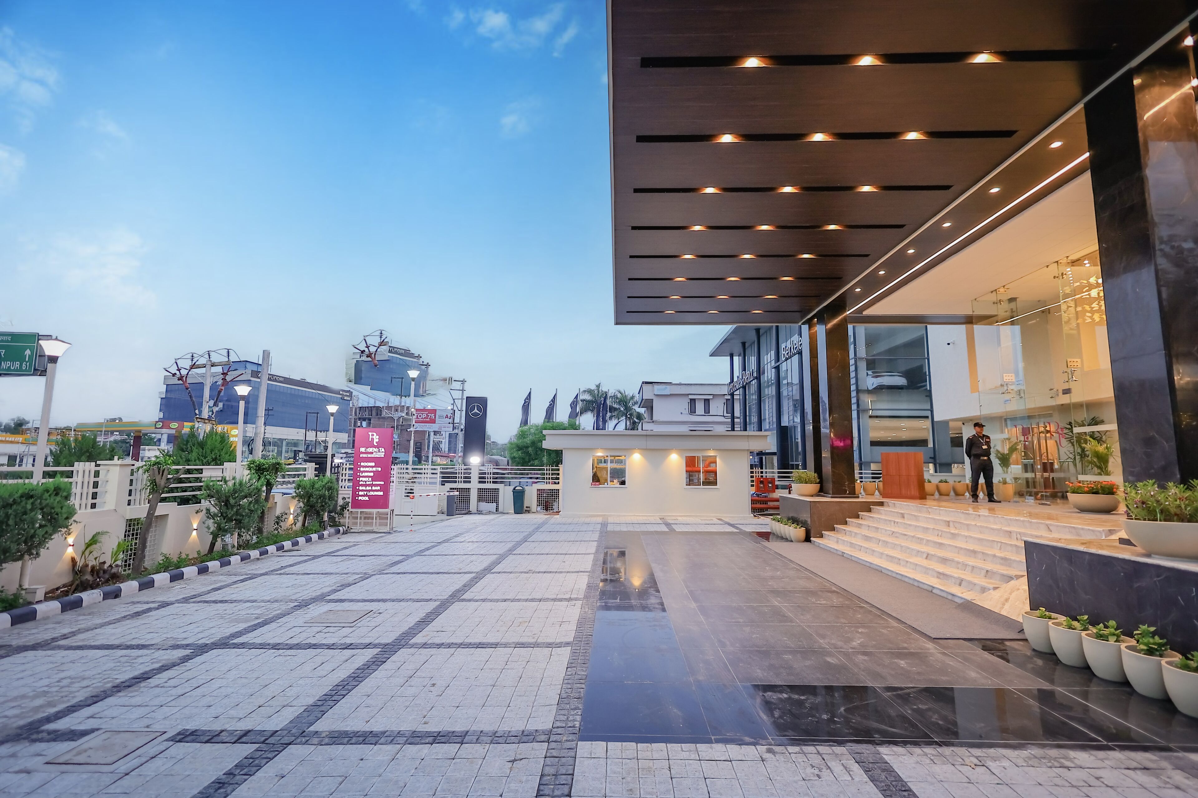 A modern hotel entrance with a glass facade, a small reception area, and a staircase leading to the lobby.