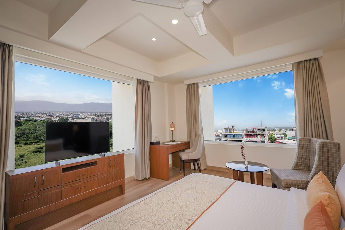 A hotel room with a large bed, a desk, a chair, and a TV.