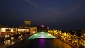 Ein moderner Poolbereich im Freien mit Bar und Sitzgelegenheiten, umgeben von beleuchteten Bäumen.