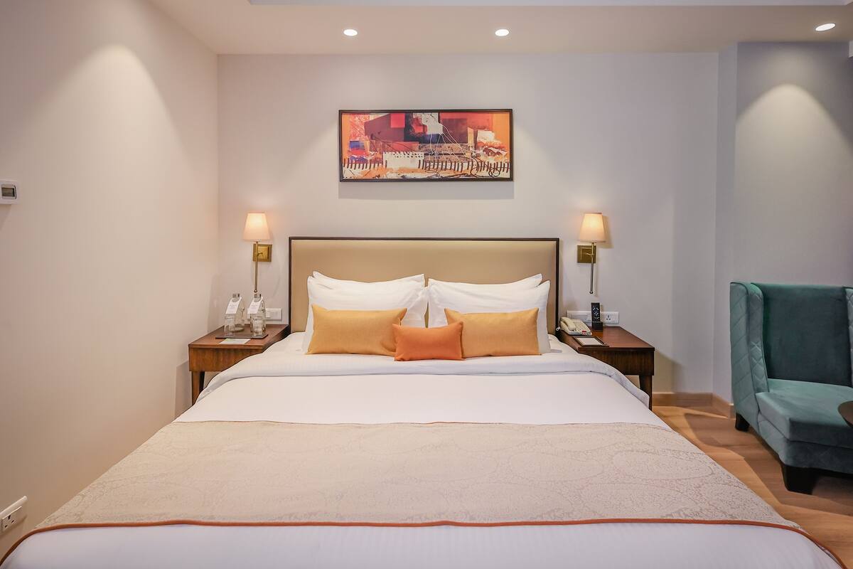 A hotel room with a large bed, two bedside tables with lamps, a green armchair, and a painting on the wall.