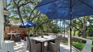 An outdoor patio with wicker furniture, a grill, and a blue umbrella. - Gorgeous newly renovated home w/ private pool and pool table w/ lagoon views. (Hilton Head Island)