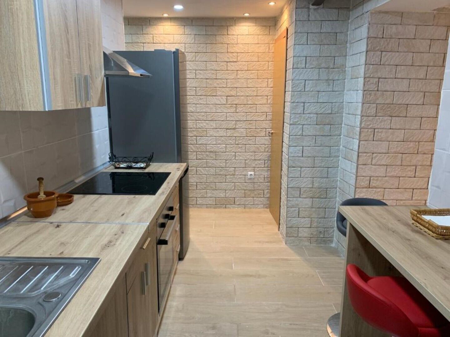 A compact kitchen with a modern design, featuring a built-in stove, a dark-colored refrigerator, and a wooden countertop.