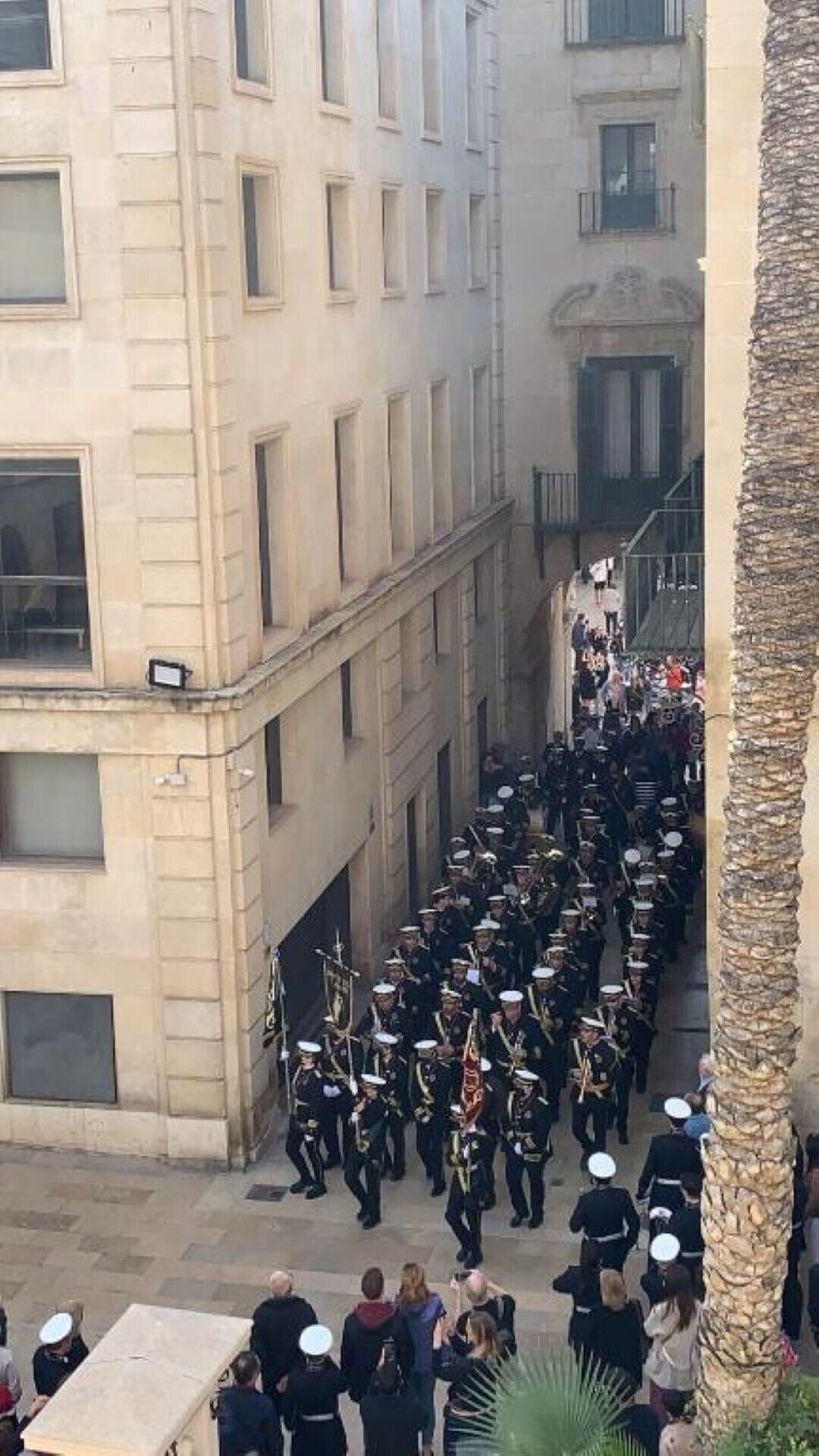 A group of uniformed personnel marching in a narrow street flanked by buildings.