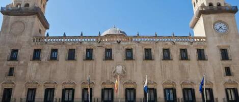 A large, historic building with two clock towers, a central dome, and multiple flags.