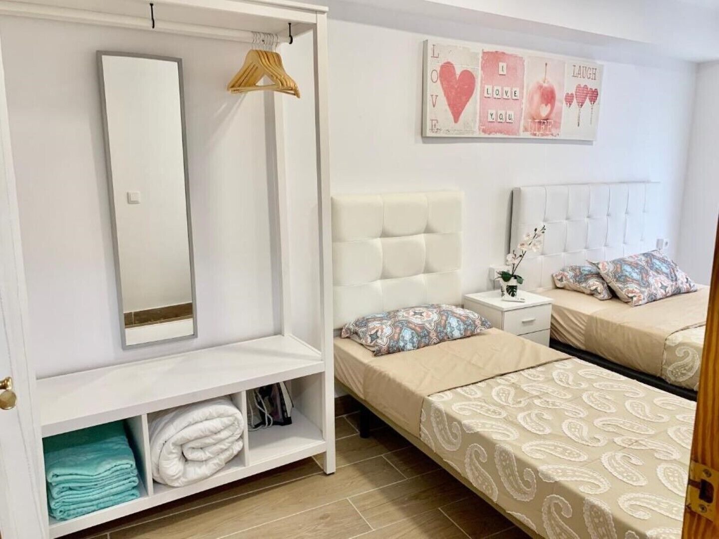 Une chambre avec deux lits, une armoire, un miroir et un élément décoratif mural.