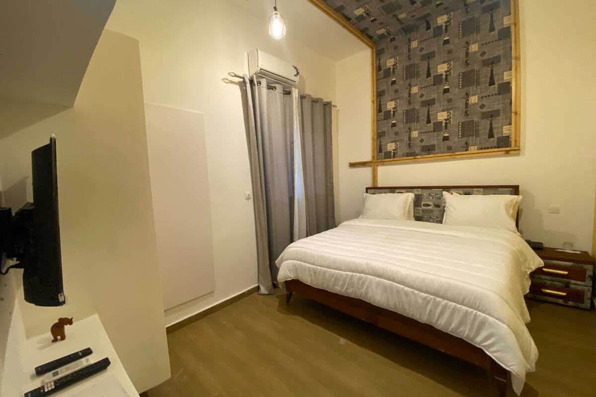 A bedroom with a bed, a TV, a wardrobe, and a patterned ceiling.