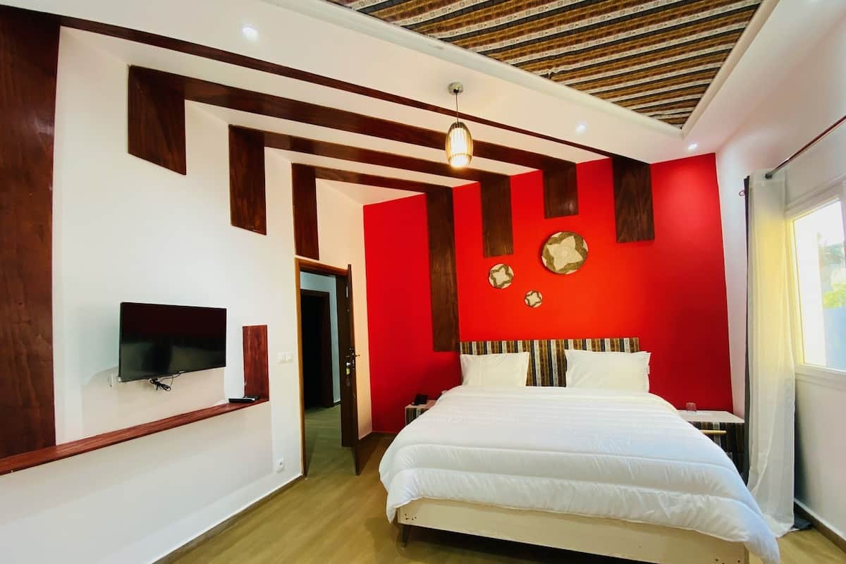 A modern bedroom with a bed, a TV mounted on the wall, and a red accent wall.