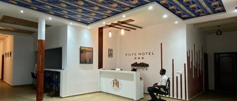 A hotel reception area with a modern design, including a patterned ceiling and a reception desk with a sign reading "Filys Hotel".