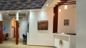A reception area with a white desk, a framed picture on the wall, and a ceiling with a blue and yellow pattern. - FILYS HÔTEL (St. Louis)