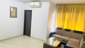 A modern living room with a glass coffee table, a sofa, a door, and an air conditioning unit. - Hotel Grand Sai - Moradabad, Uttar Pradesh (Moradabad)
