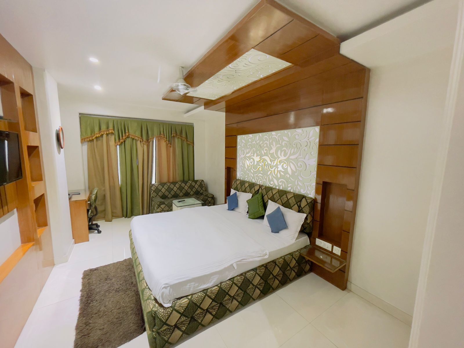 Una camera d'albergo moderna con un letto grande, un divano, una televisione e una ventola a soffitto.