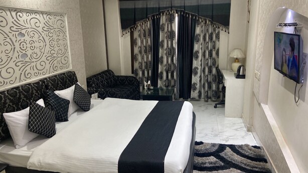 A hotel room with a large bed, a sofa, a desk, and a TV. - Hotel Grand Sai - Moradabad, Uttar Pradesh (Moradabad)