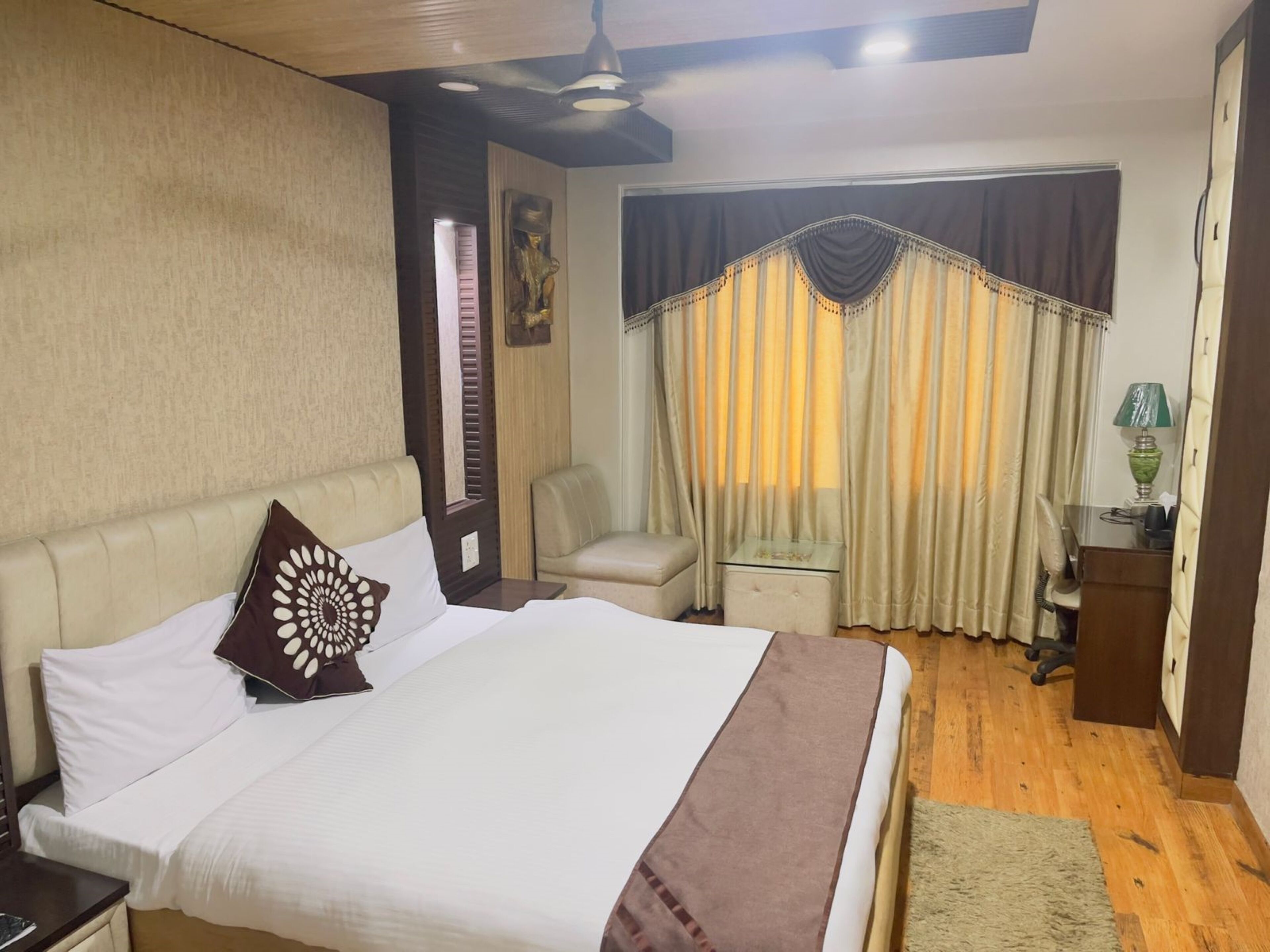 A hotel room with a bed, a desk, a chair, a lamp, and a window with curtains.
