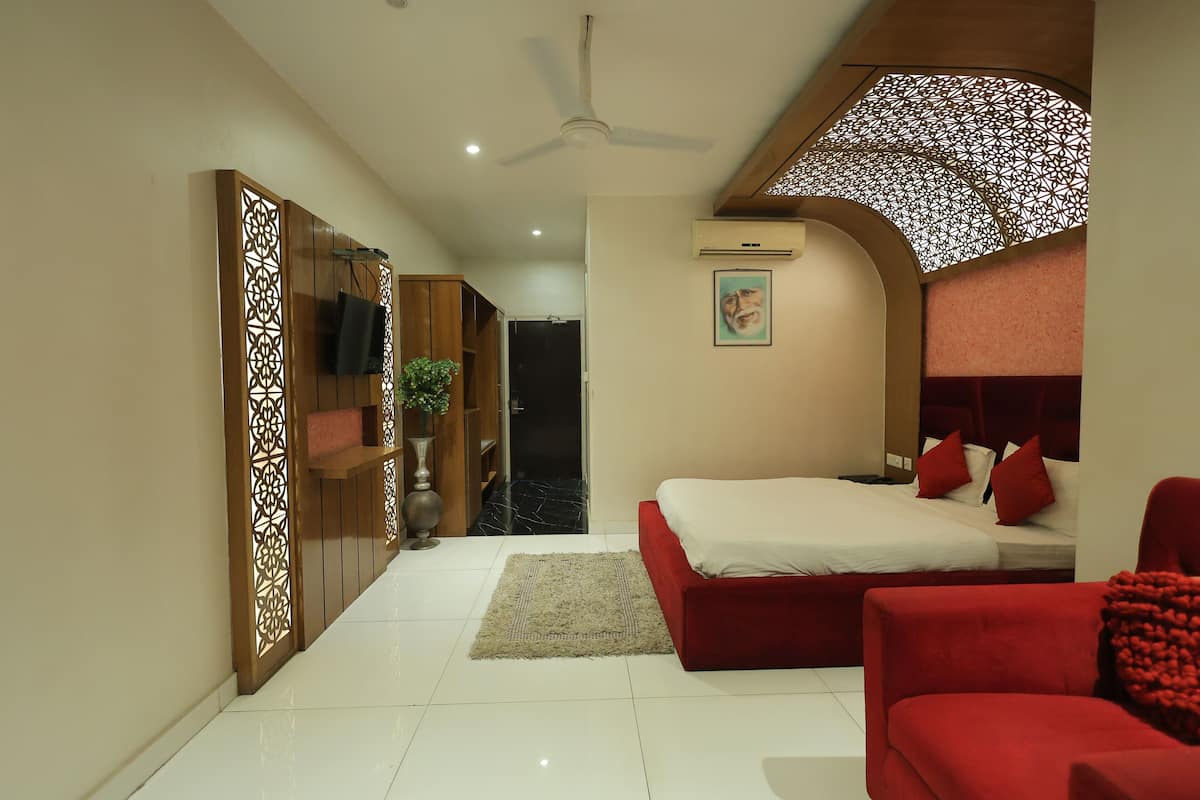 A modern bedroom with a large bed, a red sofa, a ceiling fan, and a decorative partition.