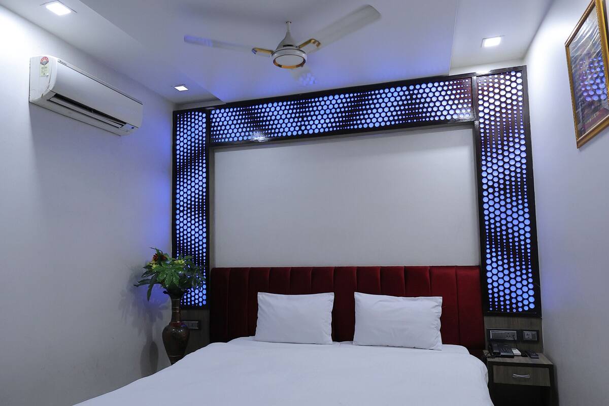 A modern hotel room with a large bed, a ceiling fan, recessed lighting, and a decorative wall panel.