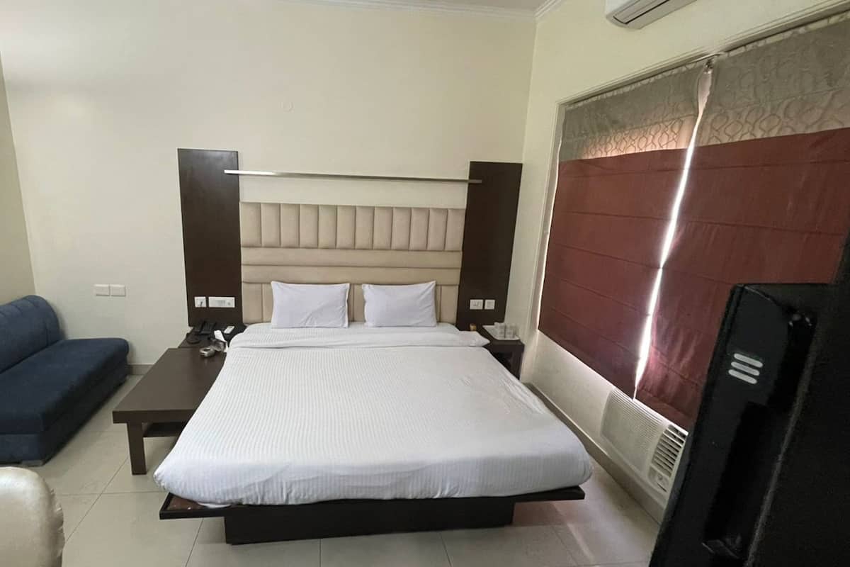 A hotel room with a bed, a bedside table with a phone, a blue sofa, and a TV.