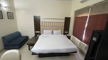 Una habitación de hotel con cama, mesita de noche con teléfono, sofá azul y televisión.