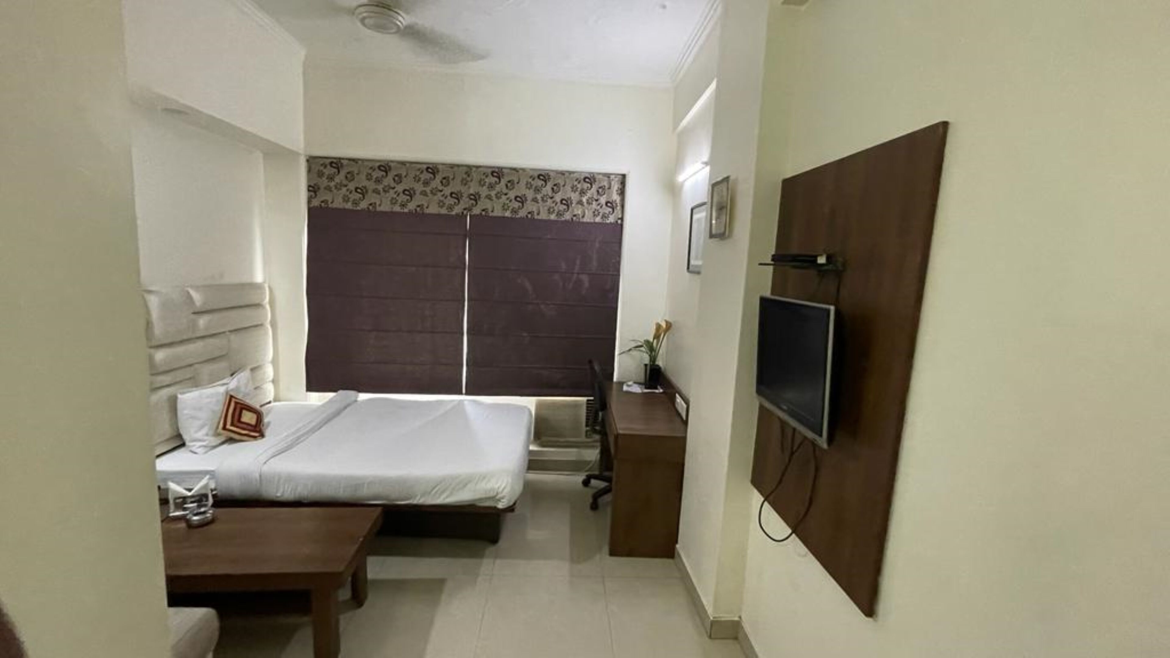 Un dormitorio con cama, mesita de noche y televisión instalada en la pared.