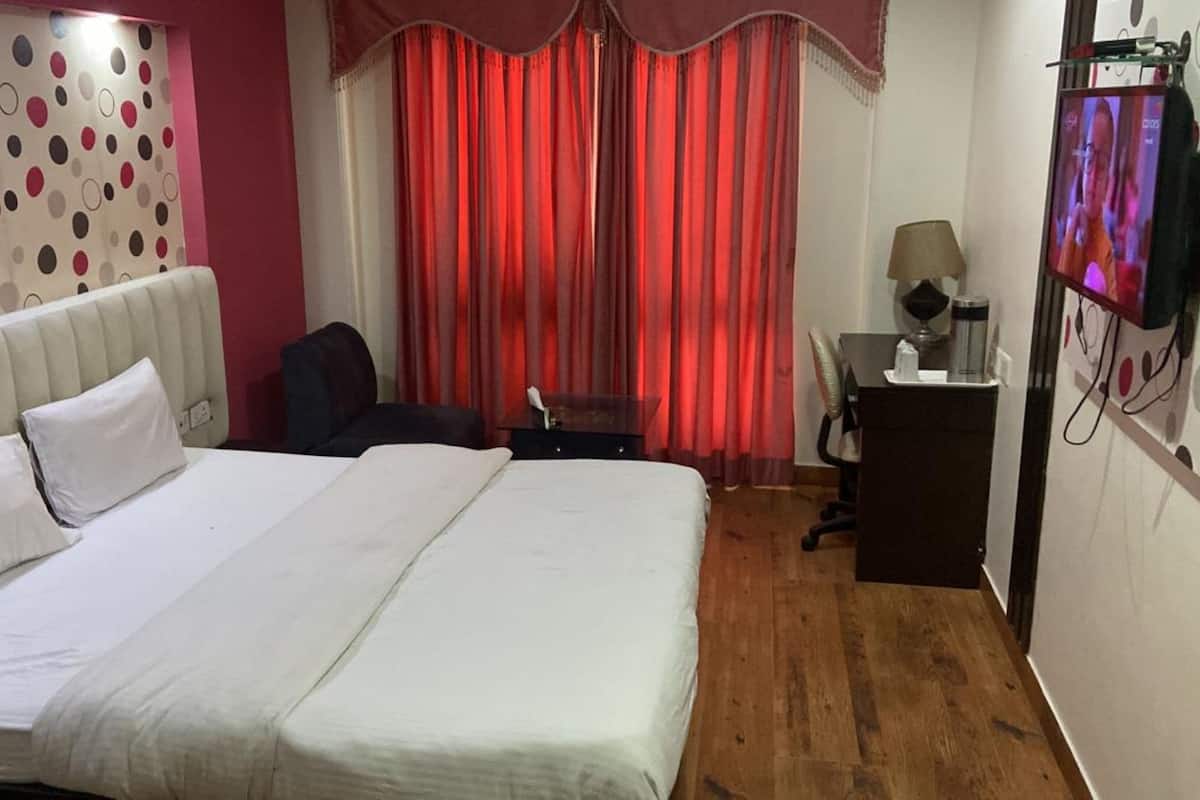 A hotel room with a bed, a desk with a chair, a TV, and a red curtain.