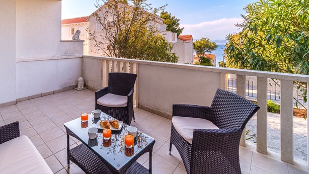 Un balcon agrémenté de meubles en osier, d’une table en verre et offrant une vue sur la mer et les bâtiments.