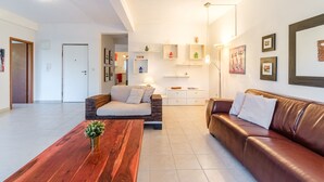 Un salon moderne avec une table basse en bois, un canapé en cuir marron et un canapé blanc. Des étagères murales sont ornées d’objets décoratifs et de tableaux encadrés.