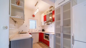 Une cuisine compacte avec des meubles blancs et rouges, un four encastré et un four à micro-ondes.
