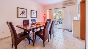 Un coin repas avec une table en bois et quatre chaises, des tableaux encadrés au mur et une vue sur les vélos garés à l’extérieur.
