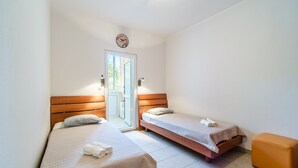 Une pièce avec deux lits, un banc en bois, un petit pouf orange et une porte donnant sur un espace extérieur.