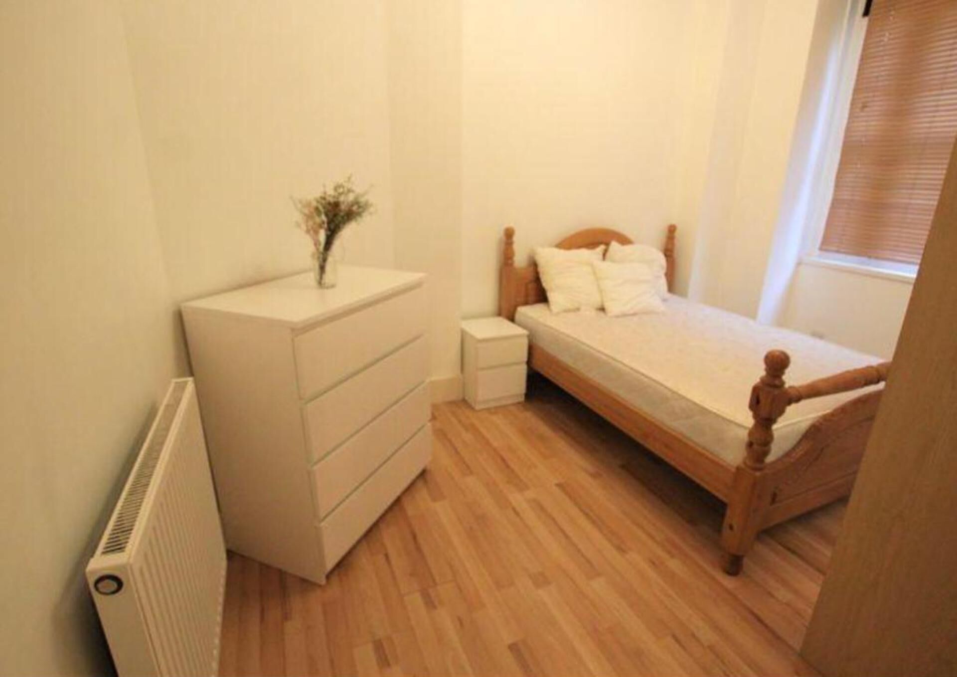 Ein Schlafzimmer mit einem hölzernen Bett, einer weißen Kommode, einem Nachttisch und einer Heizung.