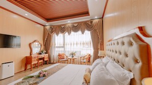 A hotel room with a large bed, a desk with a mirror, a TV, and a seating area with chairs and a table. - Tuan Nam Hotel (Hai Phong)