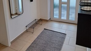 Una habitación moderna con un espejo grande, una chaqueta negra en un perchero, una alfombra blanco y negro, y un ventanal corredero que da al exterior.