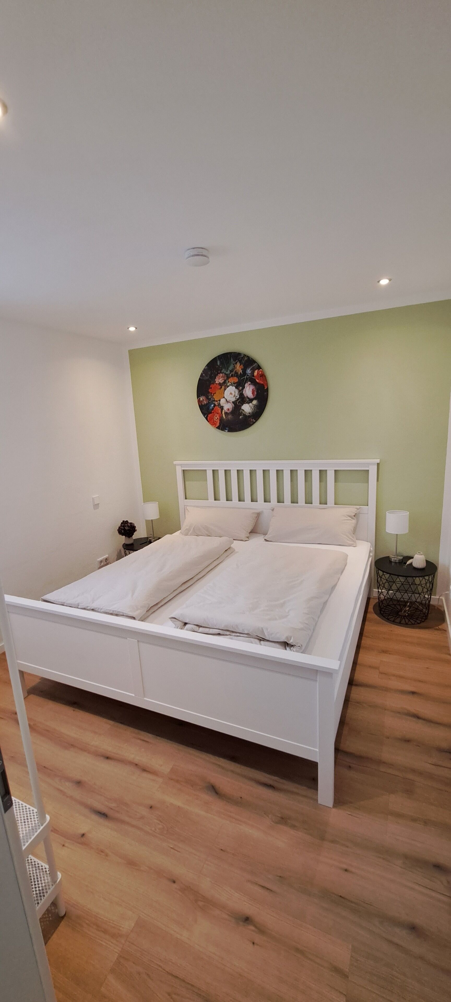 Un letto rifatto con lenzuola bianche, una decorazione rotonda a parete e un comodino con una lampada.