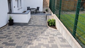 Un patio con suelo de baldosas, una mesa pequeña y sillas, y una planta en maceta.