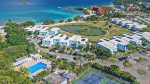 A coastal resort with multiple blue-roofed buildings, a central circular water feature, and a tennis court.