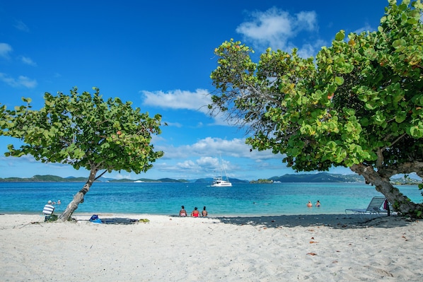 A beach with a clear blue sky, a boat in the distance, and people swimming. - The View at Crystal Cove Sapphire Beach- Beachfront Property at SBCW (St. Thomas, VI)