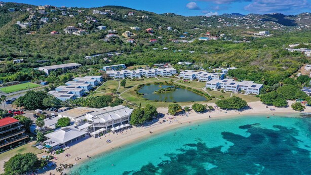 An aerial view of a resort with multiple buildings, a beach, and a clear blue sea.