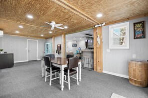 A room with a wooden ceiling, a dining table with chairs, a kitchen area, and a barrel. - Rare NMB Gem | Perfect for Groups | Great Location | Parking for 5 (North Myrtle Beach)