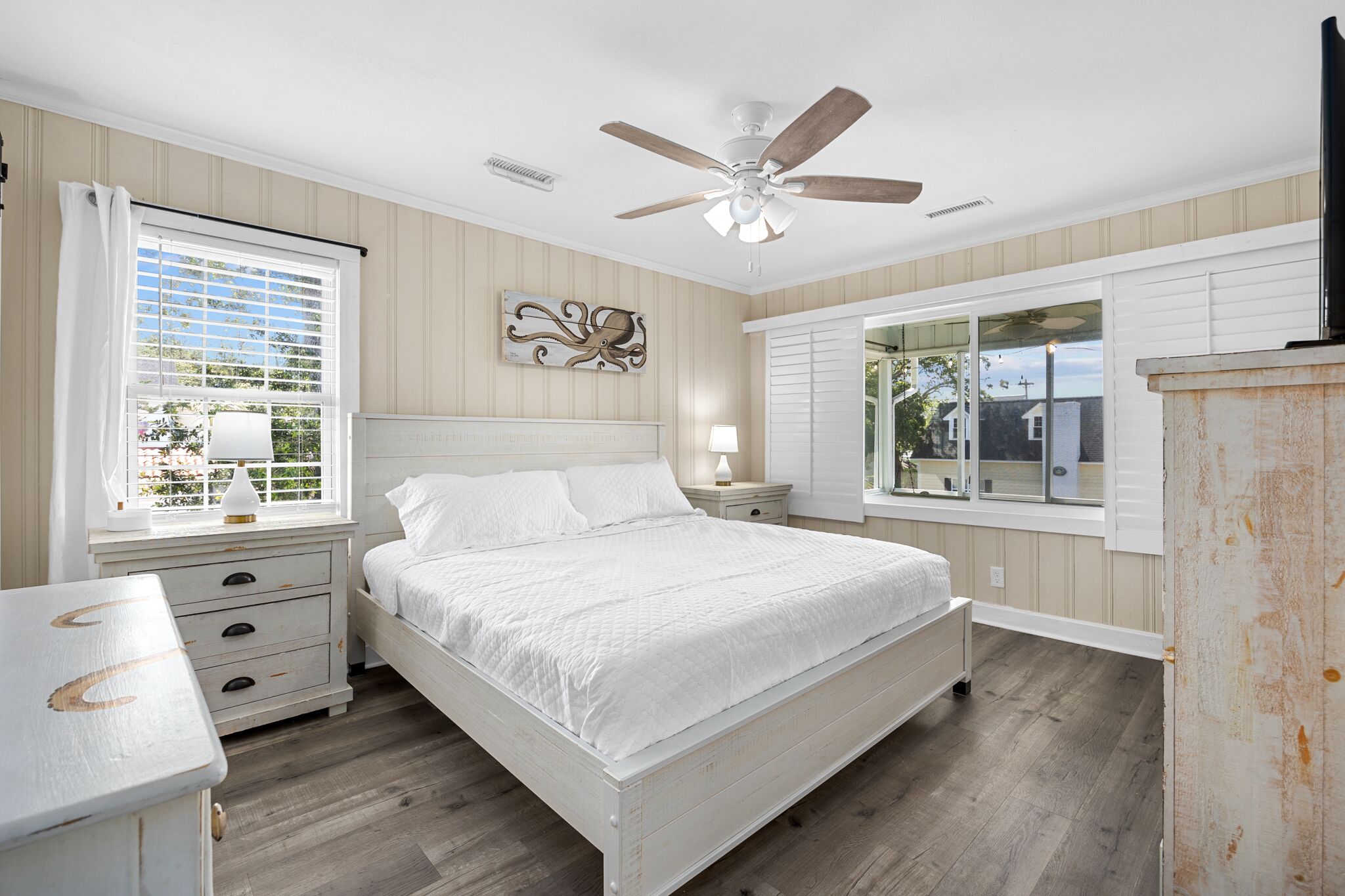 A bedroom with a bed, a nightstand, a ceiling fan, and a window with shutters.